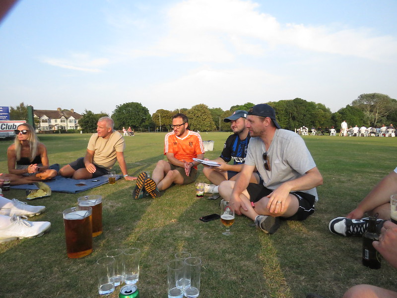 Anson players and supporters sit on the grass after the game at Harrow Lodge and enjoy a beer